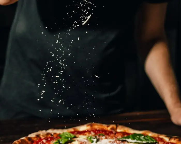 Pizzaiolo posypuje pizzę parmezanem